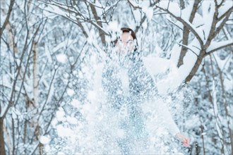 The girl is having fun in the winter forest. She sprinkles everything around with snow. Winter holiday concept. Tourism.