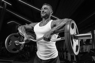 Handsome young man working out with a barbell in the gym. Shoulder pumping. Barbell pull to the chin. Fitness and bodybuilding concept