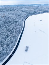A winding road runs through a wintry landscape with snow-covered fields