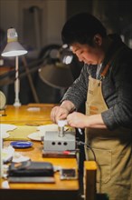 Asian Master luthier lute maker artisan both hands performing bend controller purfling strips process in iron tool for a new raw back and front plates of classic handmade violin in his workshop in Cre...