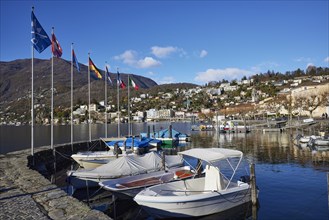 Motorboats and stone wall with flags in the harbour of Ascona