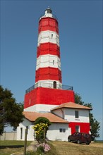 A red and white striped lighthouse next to a house with a vehicle in front of it under a clear sky