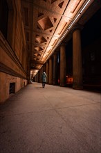 A lone person stands at night between large pillars under street lighting