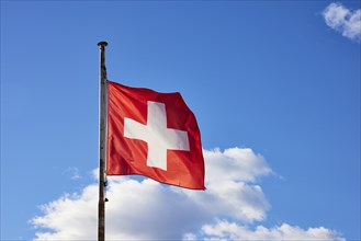 Swiss flag on a flagpole in front of a blue sky with white clouds in Ascona