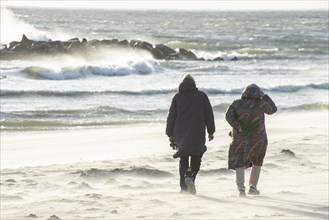 Two women walk in stormy weather along the beach in Ystad