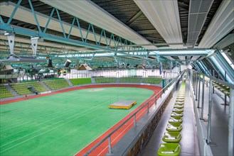 Comprehensive interior view of an empty sports hall with green rows of seats and sports field