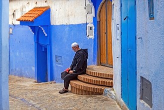 Muslim man wearing traditional djellaba in alleyway with blue houses and doors in medina