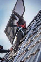 Reba worker mounts a solar panel on a roof with safety equipment