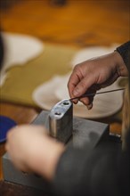 Unrecognizable luthier lute maker artisan hands in his workshop performing bend controller purfling strips process in iron tool for a new raw back and front plates of classic handmade violin in Cremon...