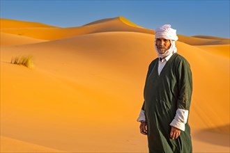 Moroccan Berber man wearing kaftan and turban in sand dunes of Erg Chebbi in the Sahara Desert near Merzouga