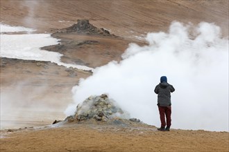 Tourist photographing steaming fumarole at Hverir