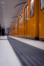 An orange underground train on a platform in a tunnel