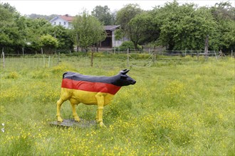 A life-size cow made of plastic in a flowering meadow