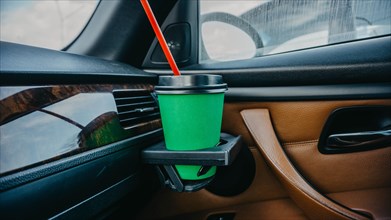 Cardboard cup of coffee inside a car in a passenger's hand