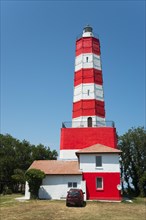 Red and white lighthouse against a clear blue sky with a red car in front of it