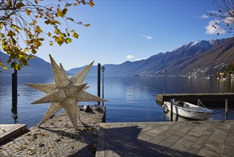 Backlit photograph of the large Herrenhuth star as a Christmas decoration at the harbour entrance to Lake Maggiore with lanterns and motorboat in Ascona