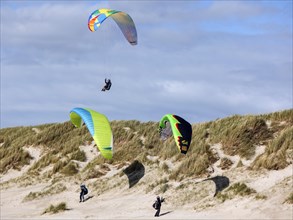 Paragliders flying over a dune landscape on a beach