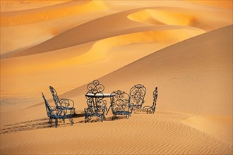 Cast iron garden table and lawn chairs in sand dunes of Erg Chebbi in the Sahara Desert near Merzouga