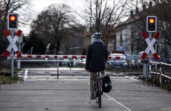 A cyclist waits at a level crossing with a barrier