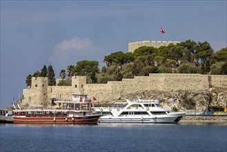 Excursion boat and yacht on the causeway to Pigeon Island in the bay of Kusadasi. A Genoese fortress towers on the summit of the island