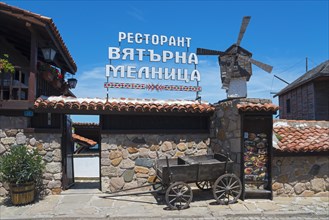 Traditional restaurant building with windmill and wooden wagon under a clear blue sky