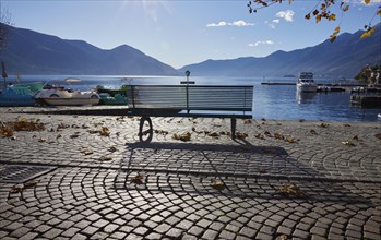 Backlit photograph of a public bench with shade and lake view on the Lungolago