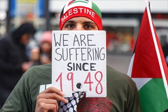 A participant in the Freedom for the People of Gaza demonstration holds a sign with the inscription We are suffering since 1948
