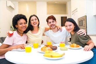 Portrait of multi-ethnic friends sitting on a breakfast table embracing and looking at camera