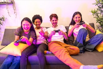 Multi-ethnic friends having fun playing console together sitting on a couch at home