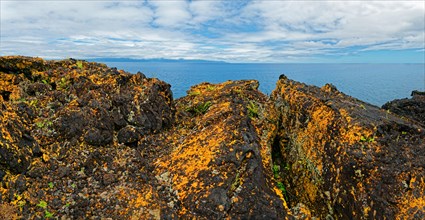 Vast landscape characterised by orange-yellow volcanic rocks, surrounded by a wide sky, lava rocks