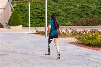Rear view of a male runner with prosthetic leg running along a park