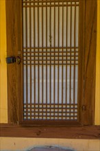 Oriental wooden slatted door of old stucco building with rice paper used for privacy on inside