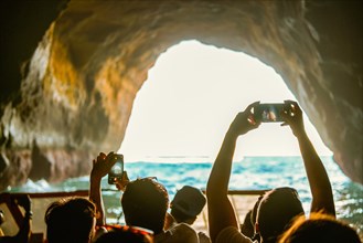 Tourist sightseeing and taking photos with smartphones inside the cave in the Algarve coast,
