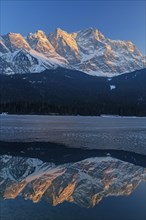 Steep mountains reflected in mountain lake in winter, icy, evening light, Eibsee lake, Zugspitze,