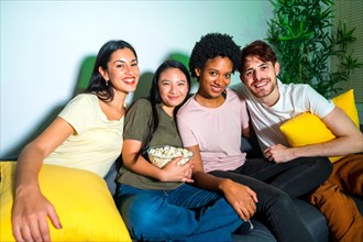 Portrait of multi-ethnic friends sitting on the sofa looking at camera ready to watch a movie