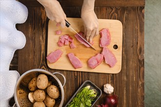 Top view of woman's hands cutting pork fillet on pieces