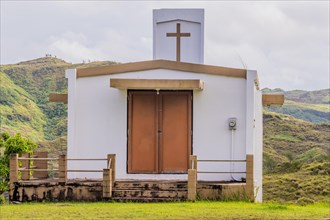 Small white country church in Guam on a hillside with mountains and a cloudy sky in the background