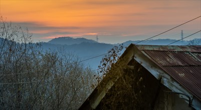 Old house with rusted tin roof with sun setting behind mountains bouncing off the atmosphere and