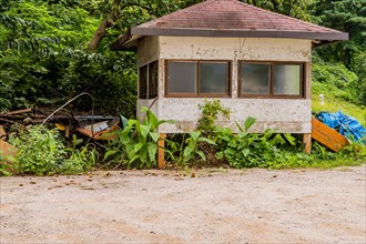 Abandoned cabin with gravel parking lot in foreground and thick vegetation in background