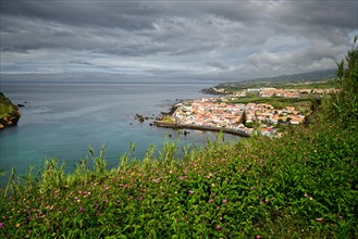 View of the town of Horta surrounded by green hills and cliffs under a cloudy sky, Monte da Guia,