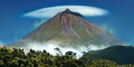 Pico volcano with a lenticularis cloud in the blue sky, surrounded by vegetation, Gruta das Torres,