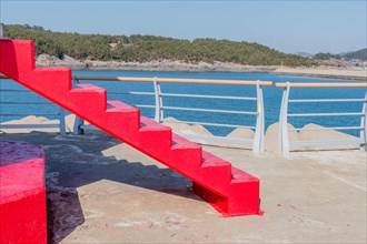Red concrete stair at base of lighthouse with ocean in background