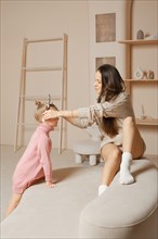 A mother and daughter are playing together in a modern living room. Daughter asks her mother to put