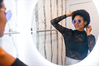 African woman with sunglasses getting ready for a night party in front of mirror