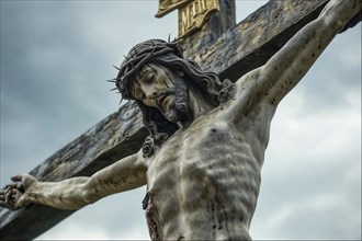 Statue of Jesus on the cross with crown of thorns under a cloudy sky, conveys a sense of suffering