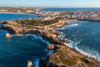 Drone view of rocky peninsula and town of Peniche, Portugal. Summer sunset haze, little foliage and