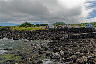Landscape with volcanic rock formations and scattered houses under a cloudy sky, lava rocks Coastal