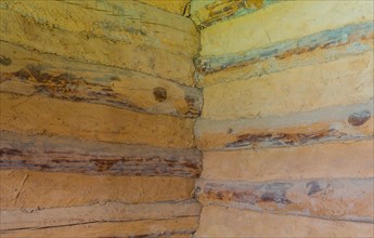 Interior corner of two walls of log cabin made of logs and held together with dried mud