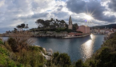 Morning sun breaking through clouds, view of the harbour entrance of Veli Losinj, with Antonius