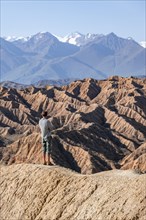 Hiker stands in front of canyons and eroded hills, Badlands, Valley of the Forgotten Rivers, near
